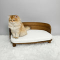 Chat assis sur un lit canapé en bois pour chat avec coussin gris dans un intérieur lumineux