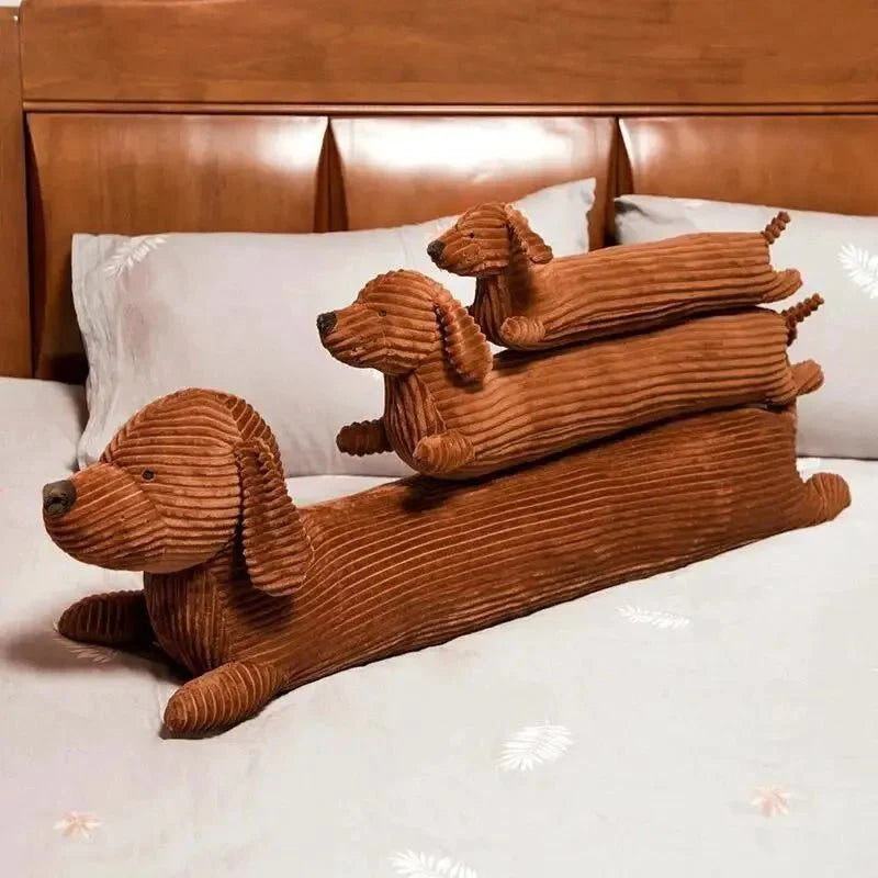 Oreiller chien teckel marron en velours côtelé de différentes tailles posé sur un lit blanc