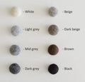 Palette de couleurs naturelles pour cocon en laine tyrolienne, incluant blanc, gris clair, gris moyen, gris foncé, beige, beige foncé, brun, et noir.